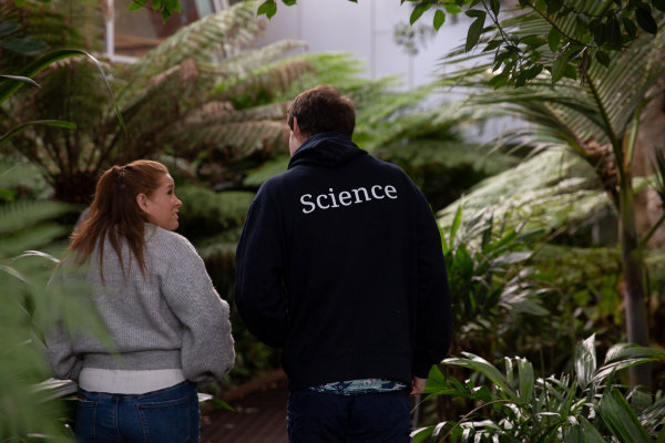 Two people walking toward a fernery, one wearing a hoodie saying 'Science' on the back.
