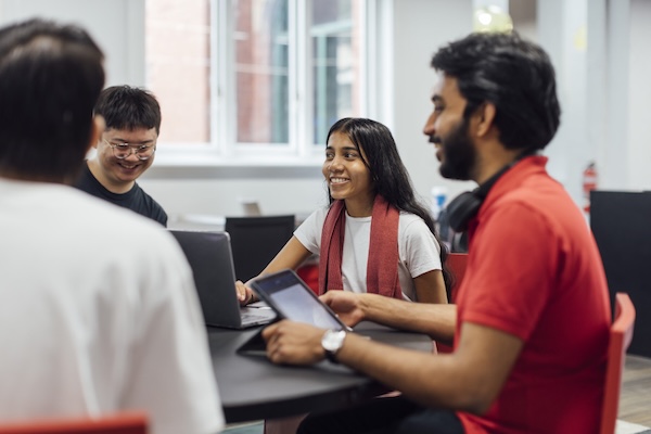 Graduate researchers and a mentor sitting around a table with laptops and tablets