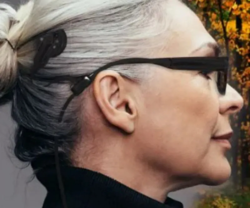Woman with bionic ear, grey hair and black framed glasses.