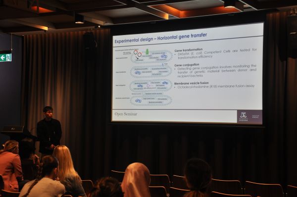 A speaker at the podium; a slide titled 'Experimental design - Horizontal gene transfer' is next to them