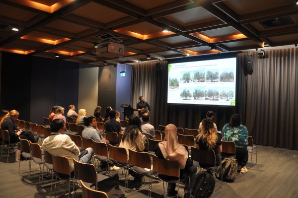 A speaker next to a slide titled 'Methodology'. Most of the audience is visible