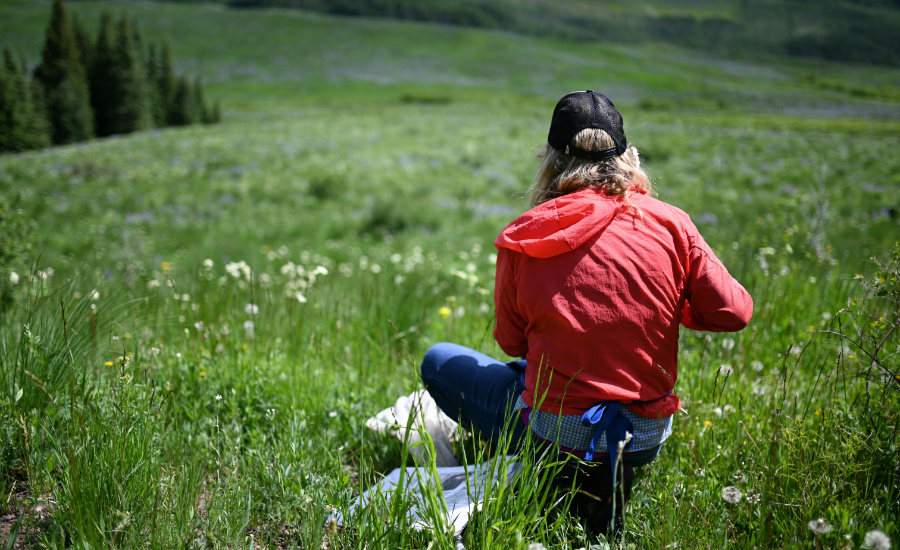 woman crouching in a field with a sample bag