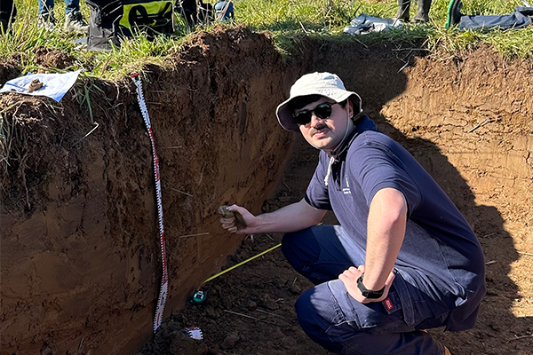 Liam crouching down in an excavation taking measurements