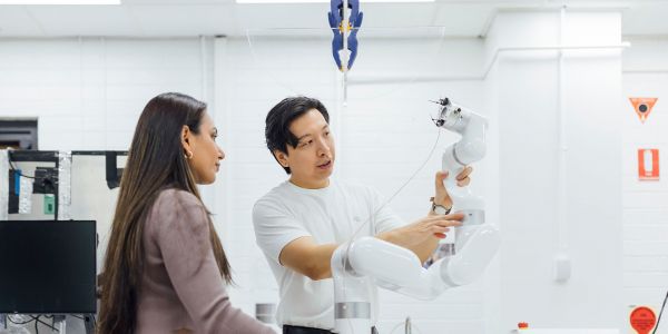 Two people looking at a robotic arm on a table