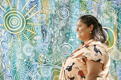 Kirsten Clark standing in profile, with her artwork behind her