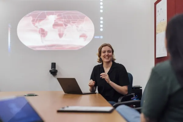 Woman giving presentation with projection of world map behind her.