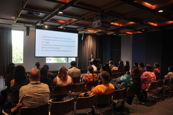 A wide-angle shot of a presentation; the speaker, slide and audience are visible