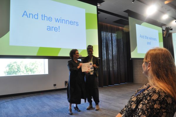 The Dean of Science presenting a certificate to a speaker in front of a slide reading 'And the winners are!'; one member of the audience is also visible