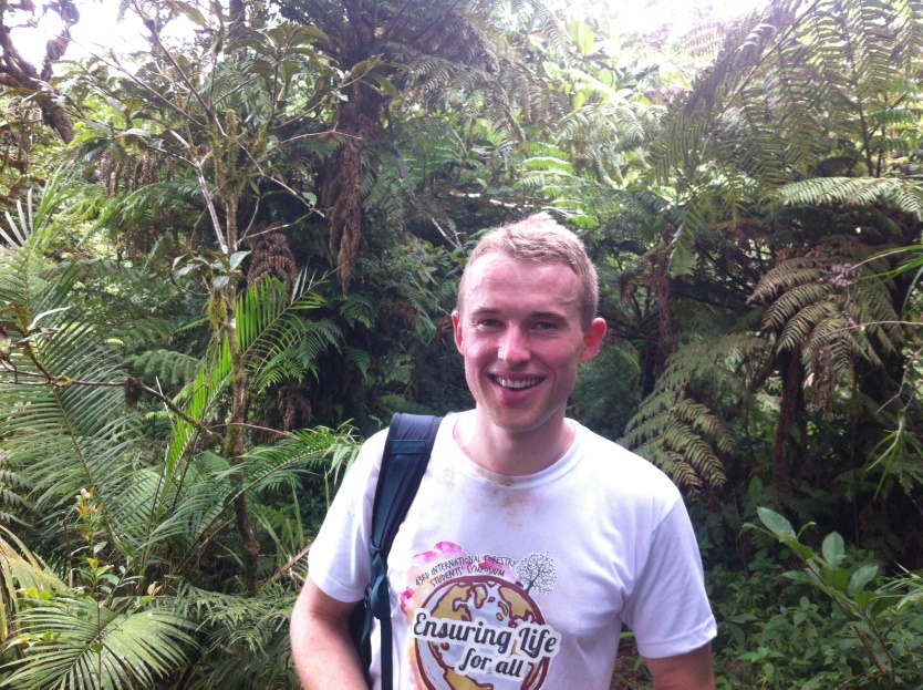 a person smiling standing in front of a rainforest