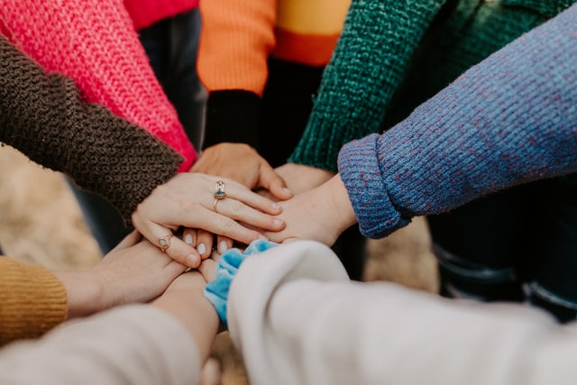 many hands in bright coloured jumpers all in together - 'hands in!'