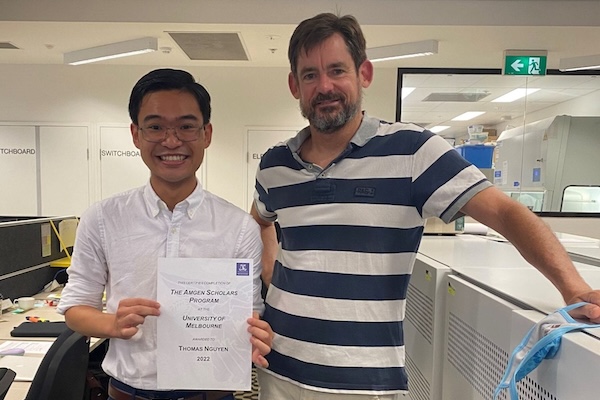 A student posing with his supervisor in a lab; the student proudly holds up a certificate showing that he has completed the Amgen program