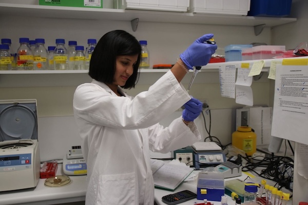 A student in a lab coat, using a pipette to mix two chemicals