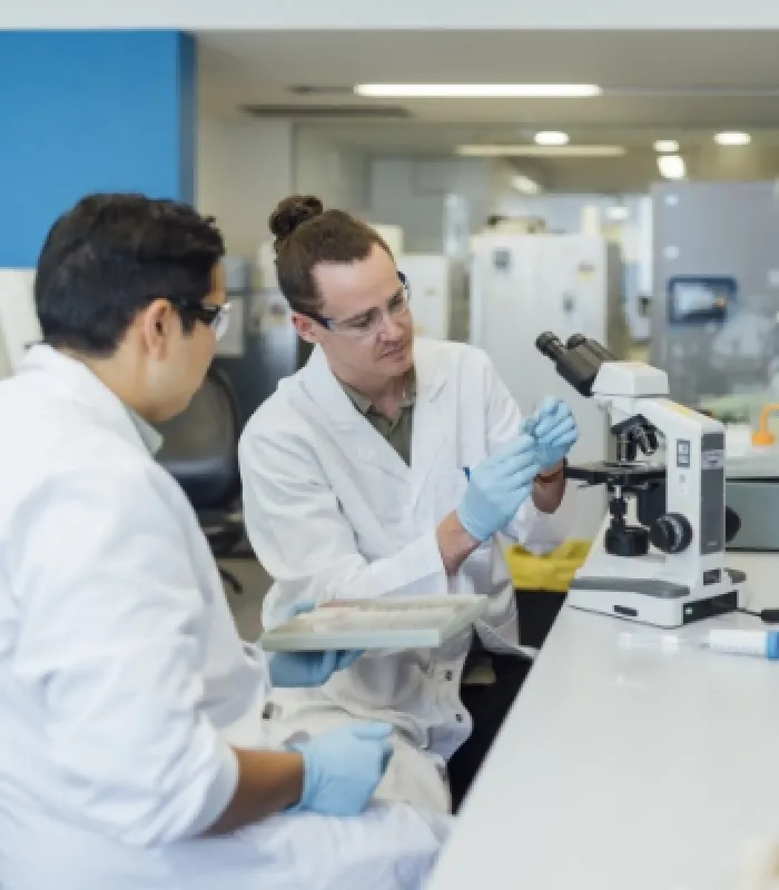 Two scientists in lab coats working at a microscrope