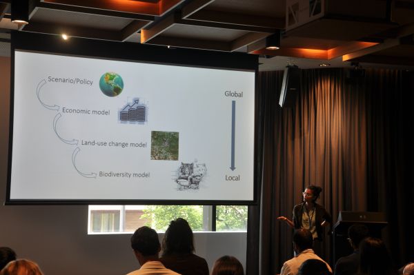 A speaker at the podium with a slide showing a flow chart next to them