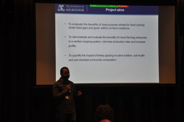 A speaker in front of a slide title 'Project aims'