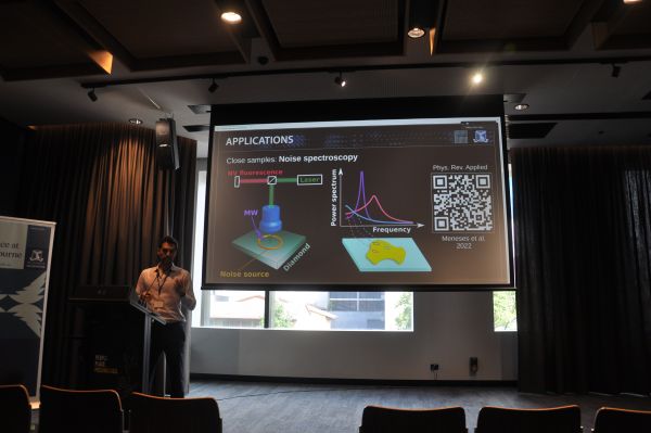A speaker at the podium next to a slide titled 'Applications'