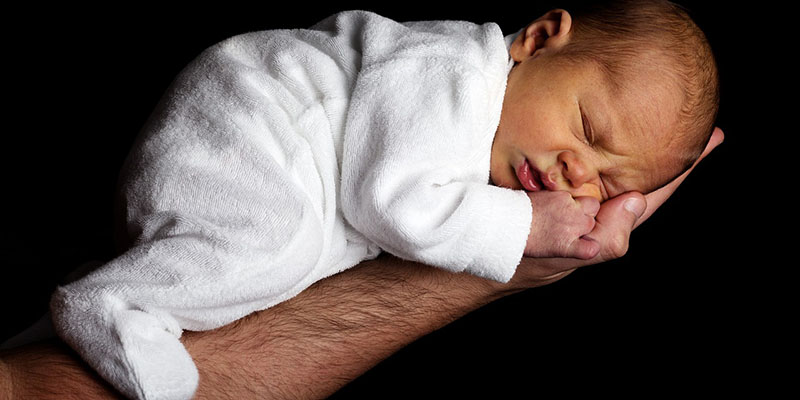 Hand/arm holding a newborn baby on its tummy