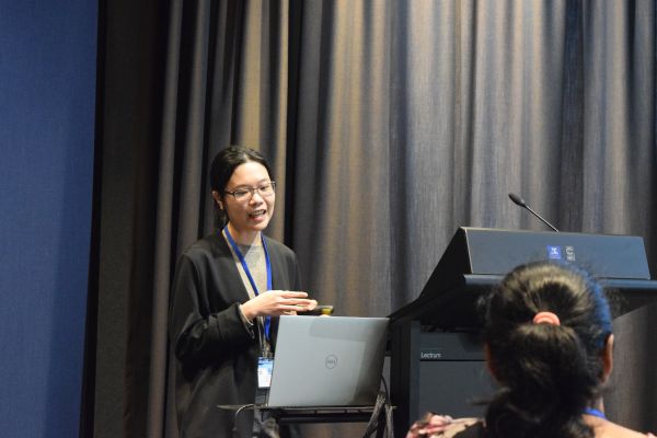 A presenter behind the podium (one audience member is also visible)