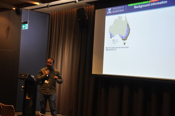 A speaker at the podium next to a slide titled 'Background information' and containing a map of Australia