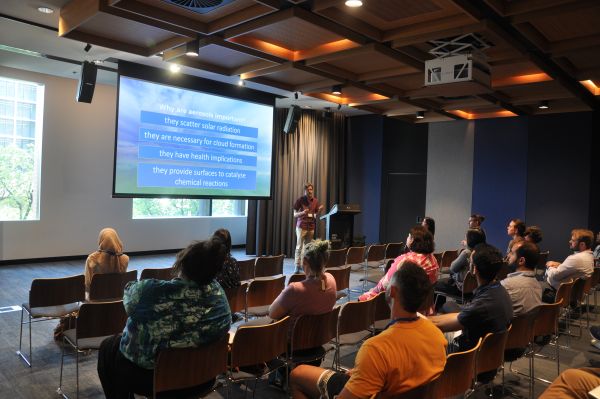 A speaker at the podium next to a slide titled 'Why are aerosols important?'; several rows of the audience are also visible