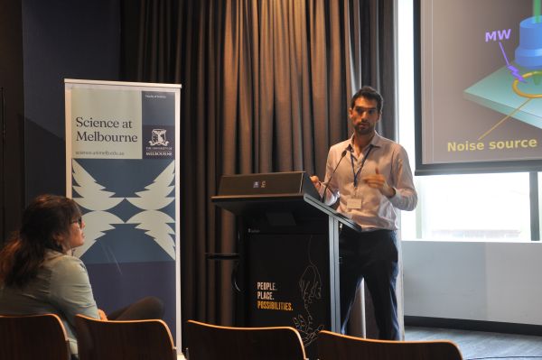 A speaker at the podium; a corner of their slide and a 'Science at Melbourne' banner are in frame
