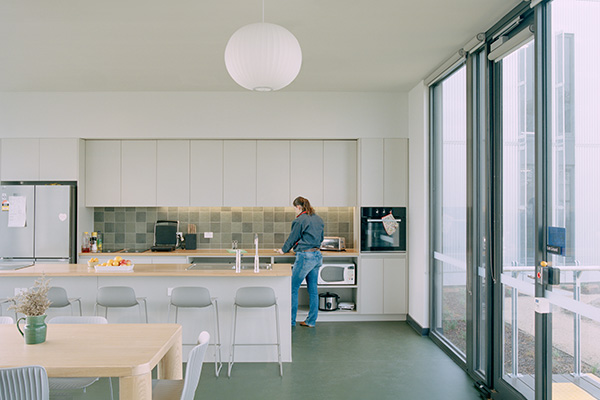 Woman works at bench in a large white kitchen with communal tables and stools