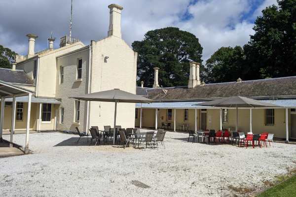 Stone courtyard full of chairs and umbrellas adjoining two story white brick building.