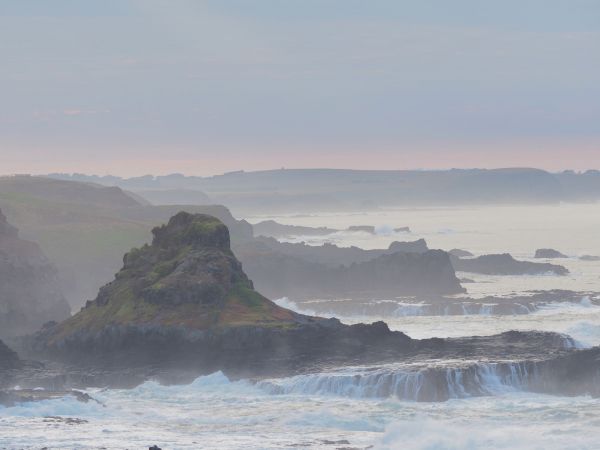 Scenic image of large pointed rock surrounded by cliffs and moving waves