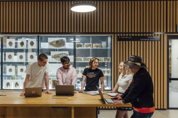Students and lecturer in discussion around a table, in front of a glass cabinet of specimens.