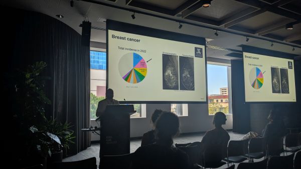 A speaker at a podium in front of a slide titled 'Breast cancer'
