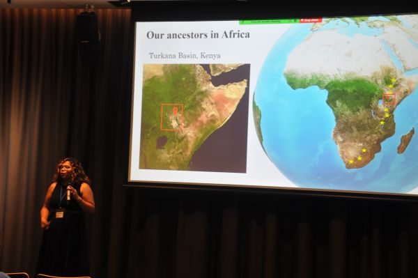 A speaker next to a slide titled 'Our ancestors in Africa' and containing several images of Africa