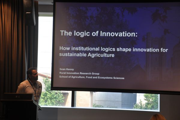 A speaker at the podium next to a slide titled 'The logic of Innovation'