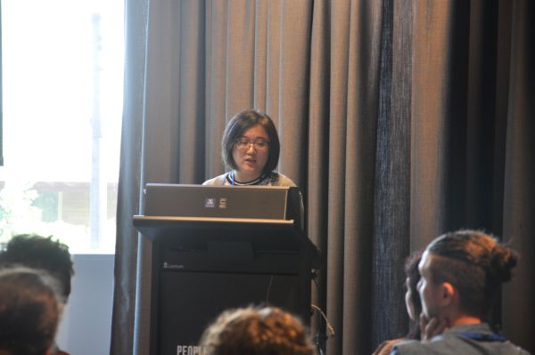 A speaker at the podium; several audience members are also partially visible