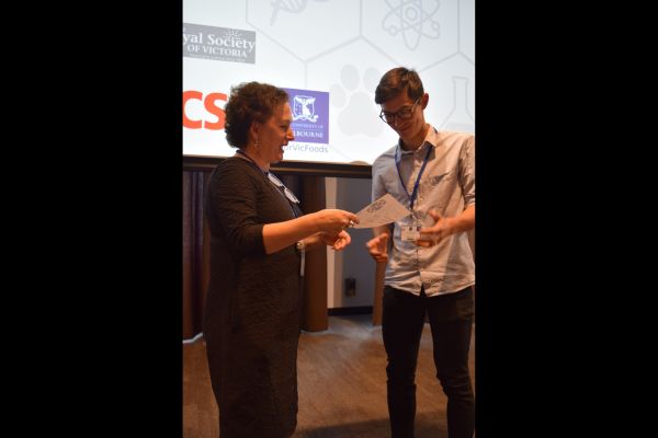 Moira O'Bryan presenting a certificate to a speaker; the bottom of a slide is visible in the background