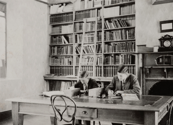 Alf Leslie (left) and Norm Endacott (1939) the student librarians sitting at a desk with bookshelves behind.