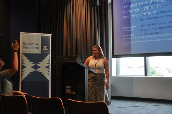 A speaker at the podium; a corner of their slide and a 'Science at Melbourne' banner are in frame
