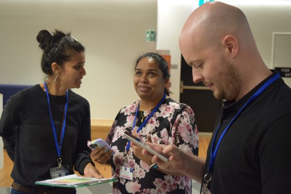 Three conference attendees, two holding smartphones and the third a clipboard