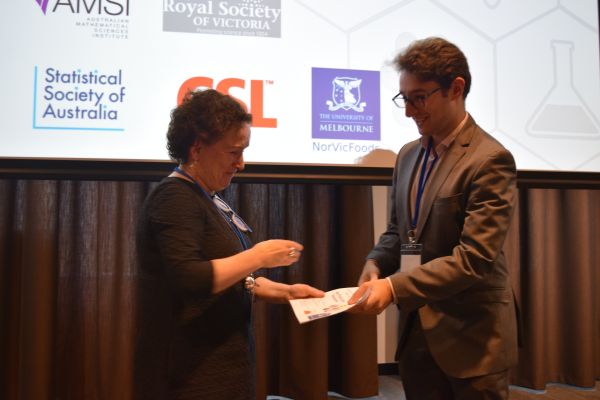 Moira O'Bryan presenting a certificate to a speaker; the bottom of a slide is visible in the background