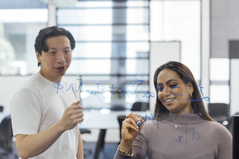 Two students write equations on a transparent screen