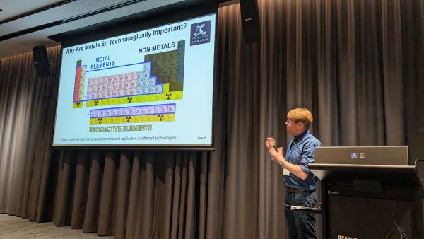 A speaker at a podium in front of a slide titled 'Why Are Metals So Technologically Important?'