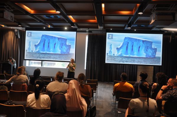 A speaker in front of slides showing an iceberg; several rows of the audience are visible