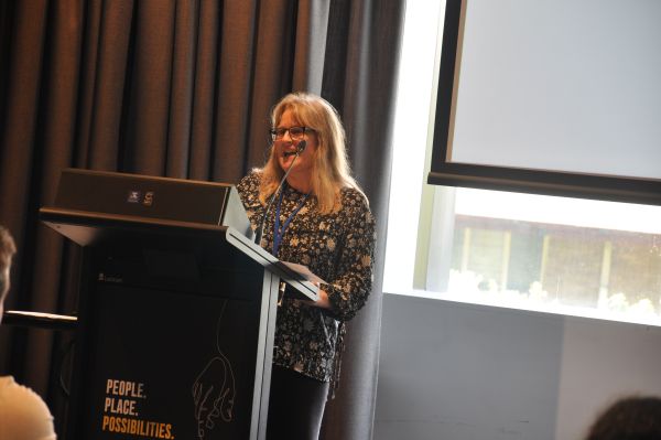 A speaker at the podium; a corner of a slide is visible