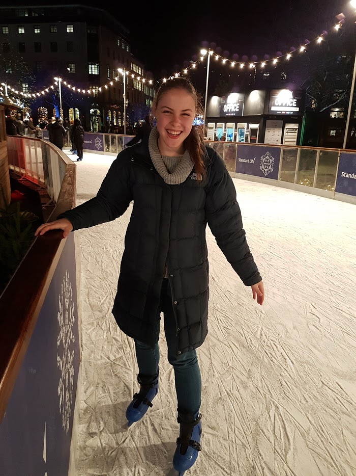 a person wearing a long coat ice skates while holding onto a rail