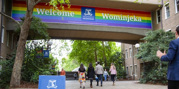 The Wominjeka / Welcome sign at the entrance to our Parkville campus - underneath, a number of students are walking away from the camera