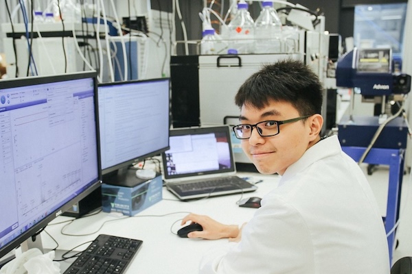 A student in a lab, sitting in front of three computer monitors