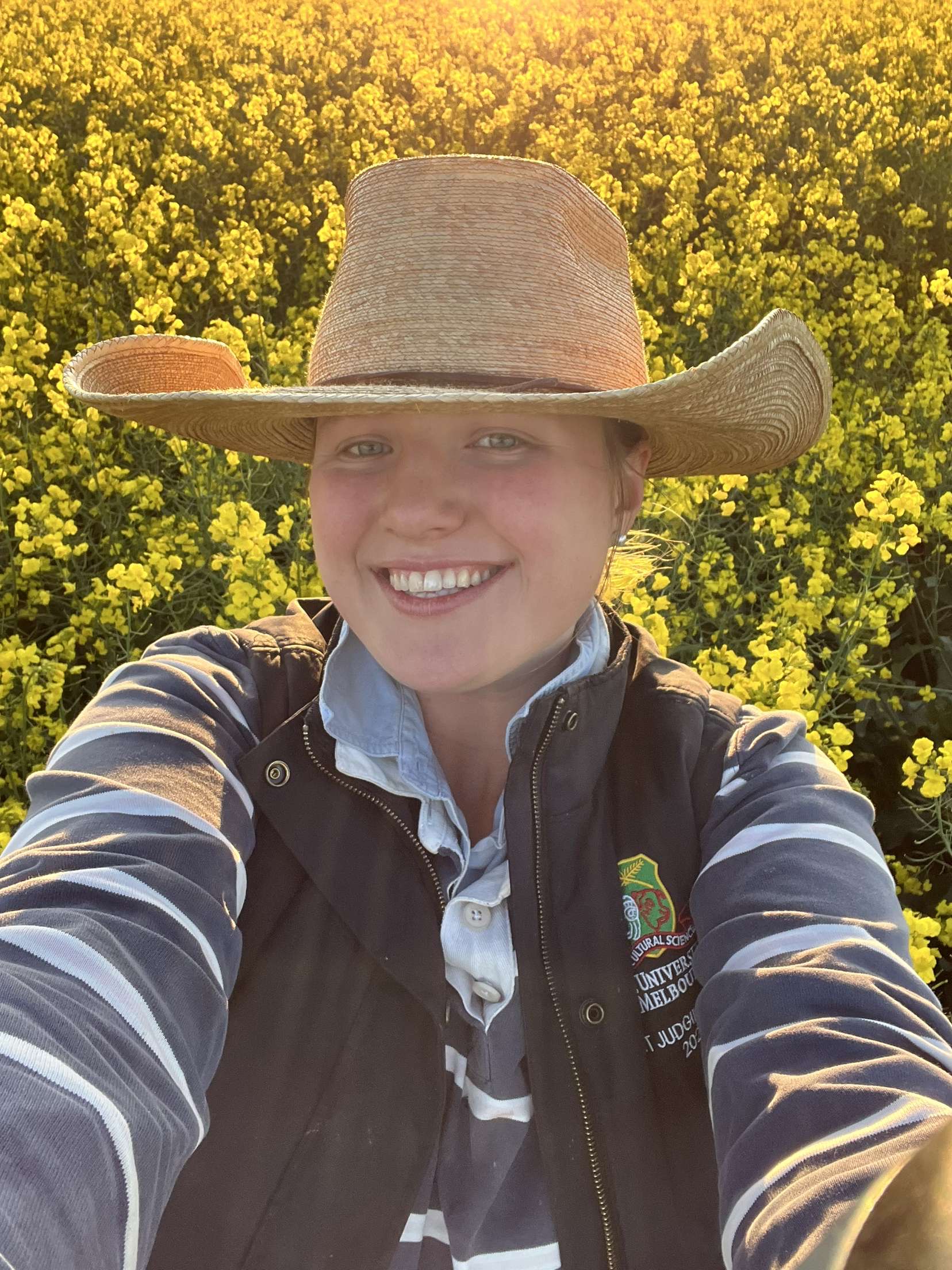 Self-taken portrait of Liza Hearmon smiling at camera in front of canola field