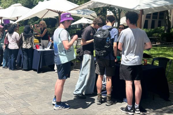 Students gathering under an umbrella at a booth at orientation