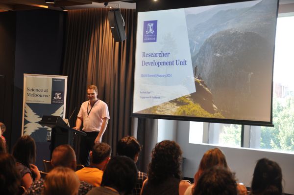 A speaker behind the podium, next to slides titled 'Researcher Development Unit'