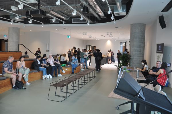 About twenty-five conference attendees talking and eating in the break area; several stalls are also visible