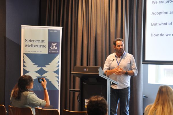 A speaker at the podium; a corner of their slide and a 'Science at Melbourne' banner can be seen